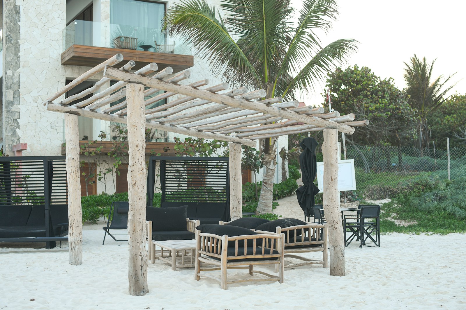 Wooden pergola with seating on a sandy beach.